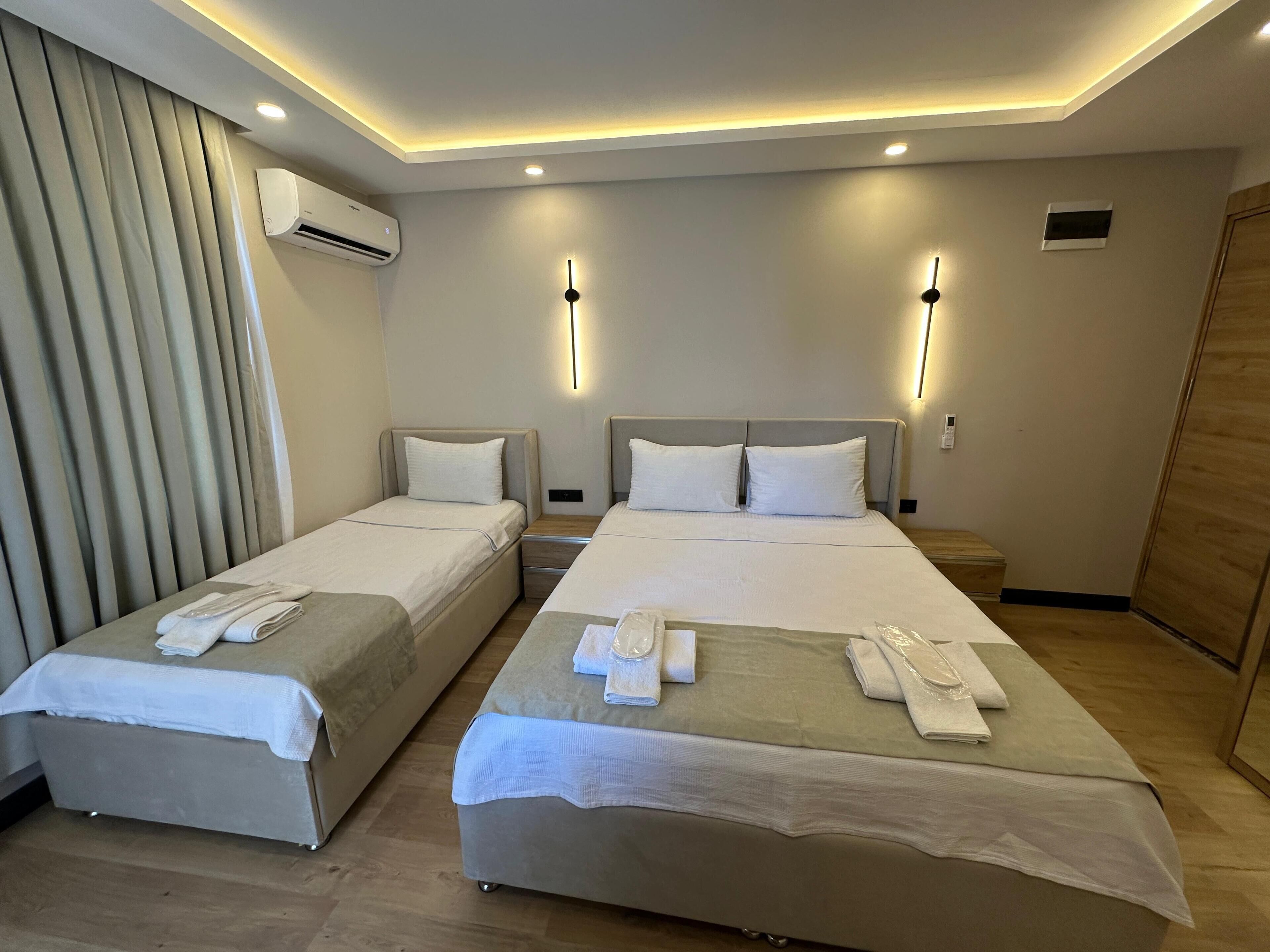 Een hotelkamer met twee bedden, een houten vloer, een airconditioning en een houten deur.