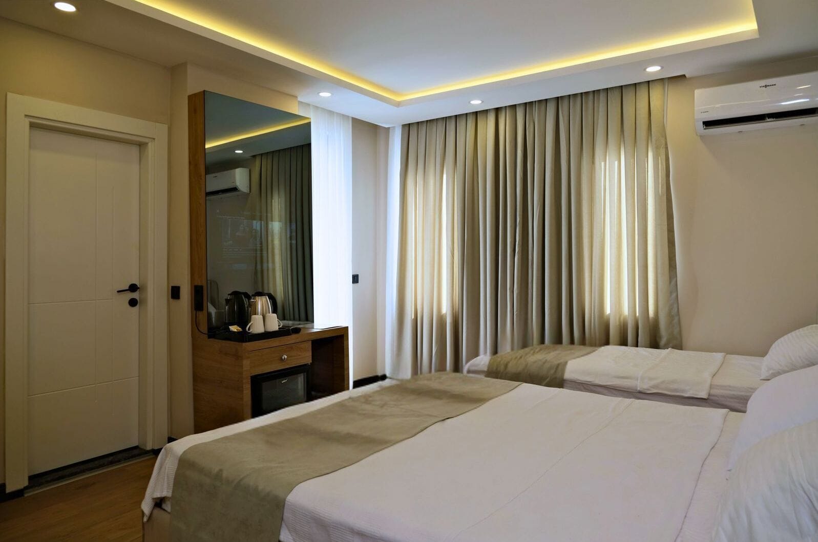 A hotel room with two beds, a desk with a coffee maker, and a large window with curtains.