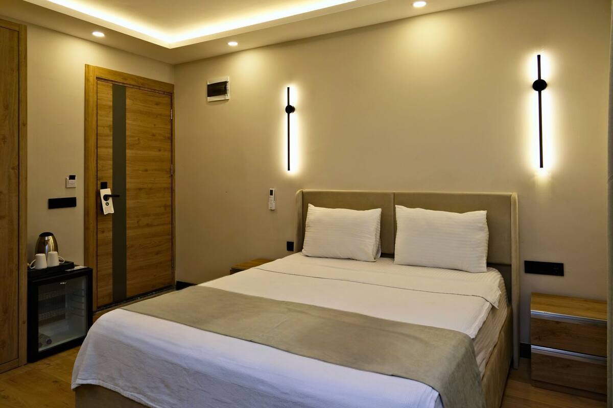 Habitació d'hotel amb un llit gran, taules de nit, un armari de fusta i aplics moderns a la paret.