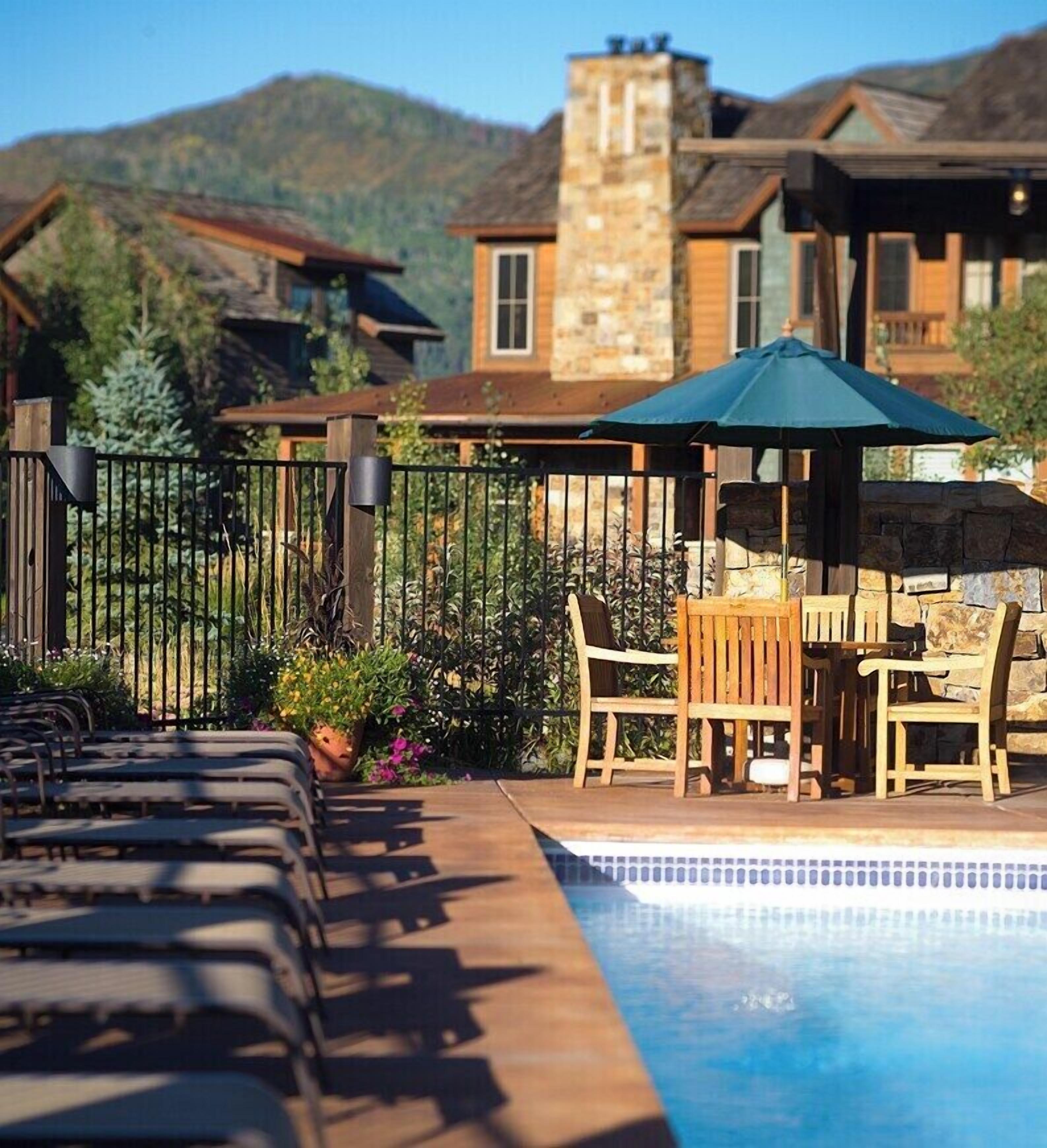 A poolside area with a wooden deck, lounge chairs, and a table with chairs.
