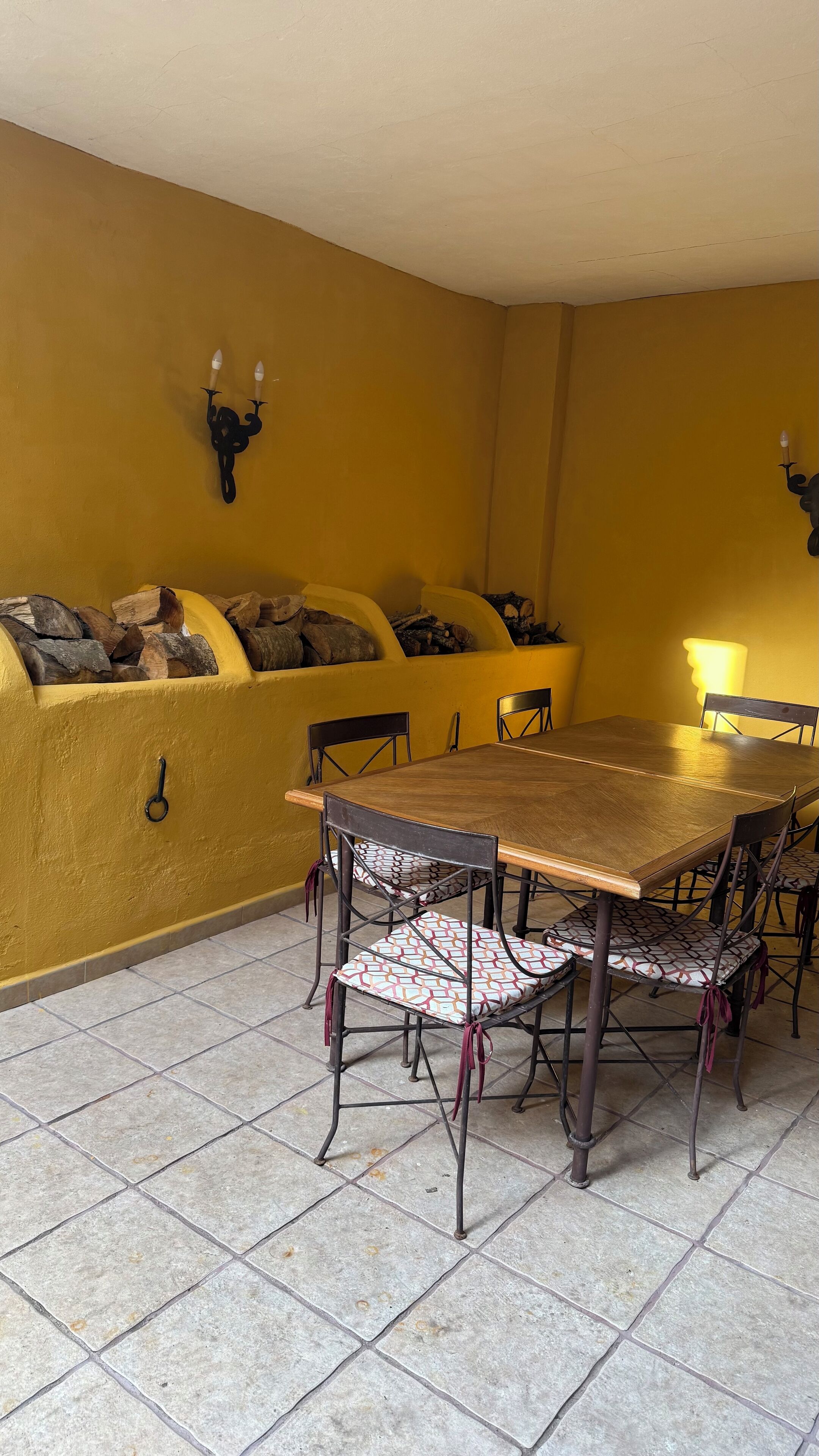 A dining area with a wooden table and chairs, a yellow wall, and a fireplace with logs.