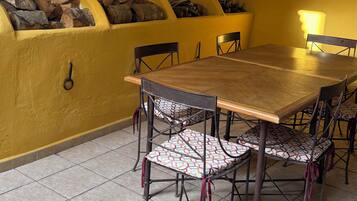 A dining area with a wooden table and chairs, a yellow wall, and a fireplace with logs.
