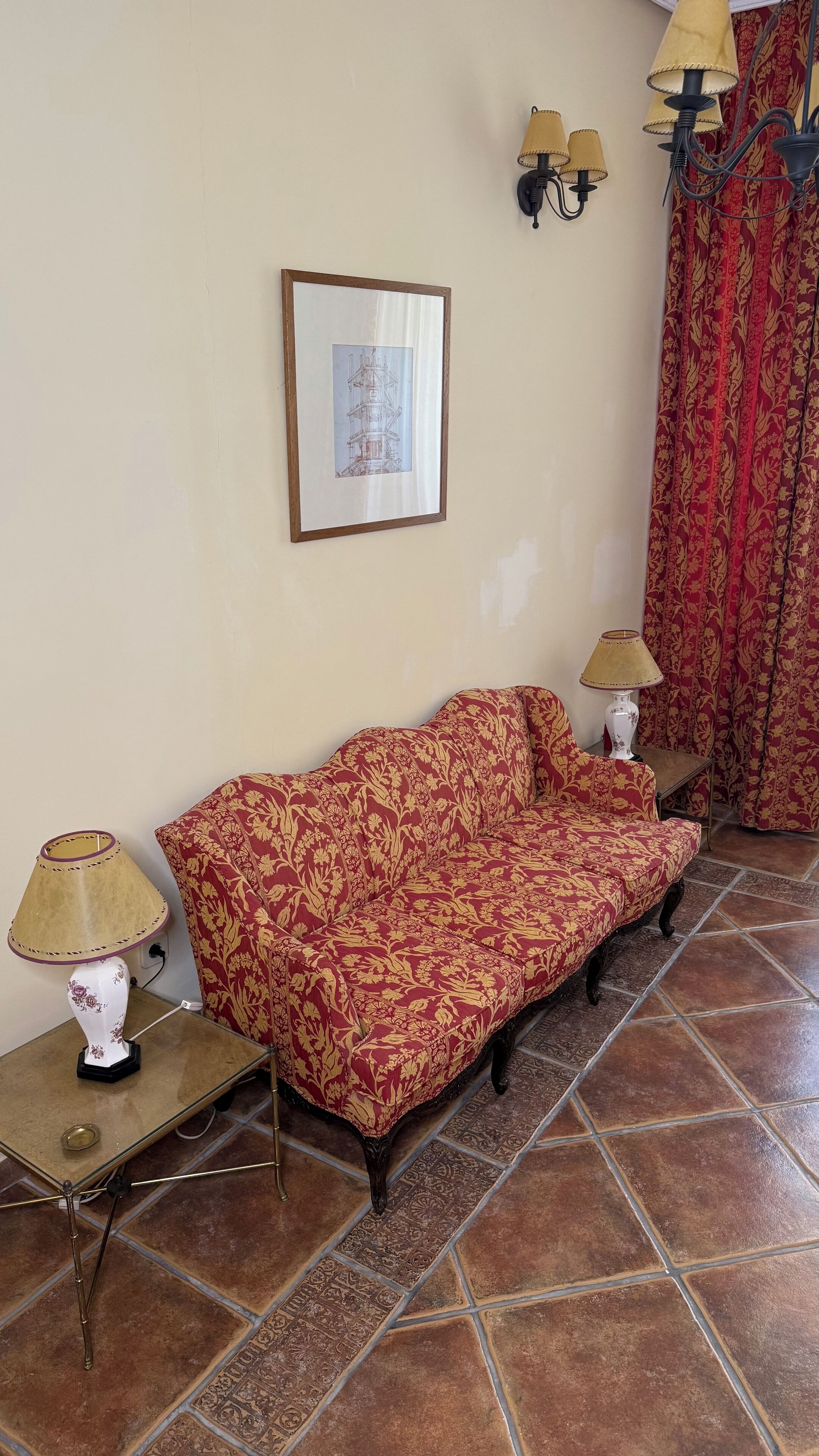 Una sala de estar con un sofá estampado, dos lámparas de pared, un cuadro enmarcado y una cortina decorada.