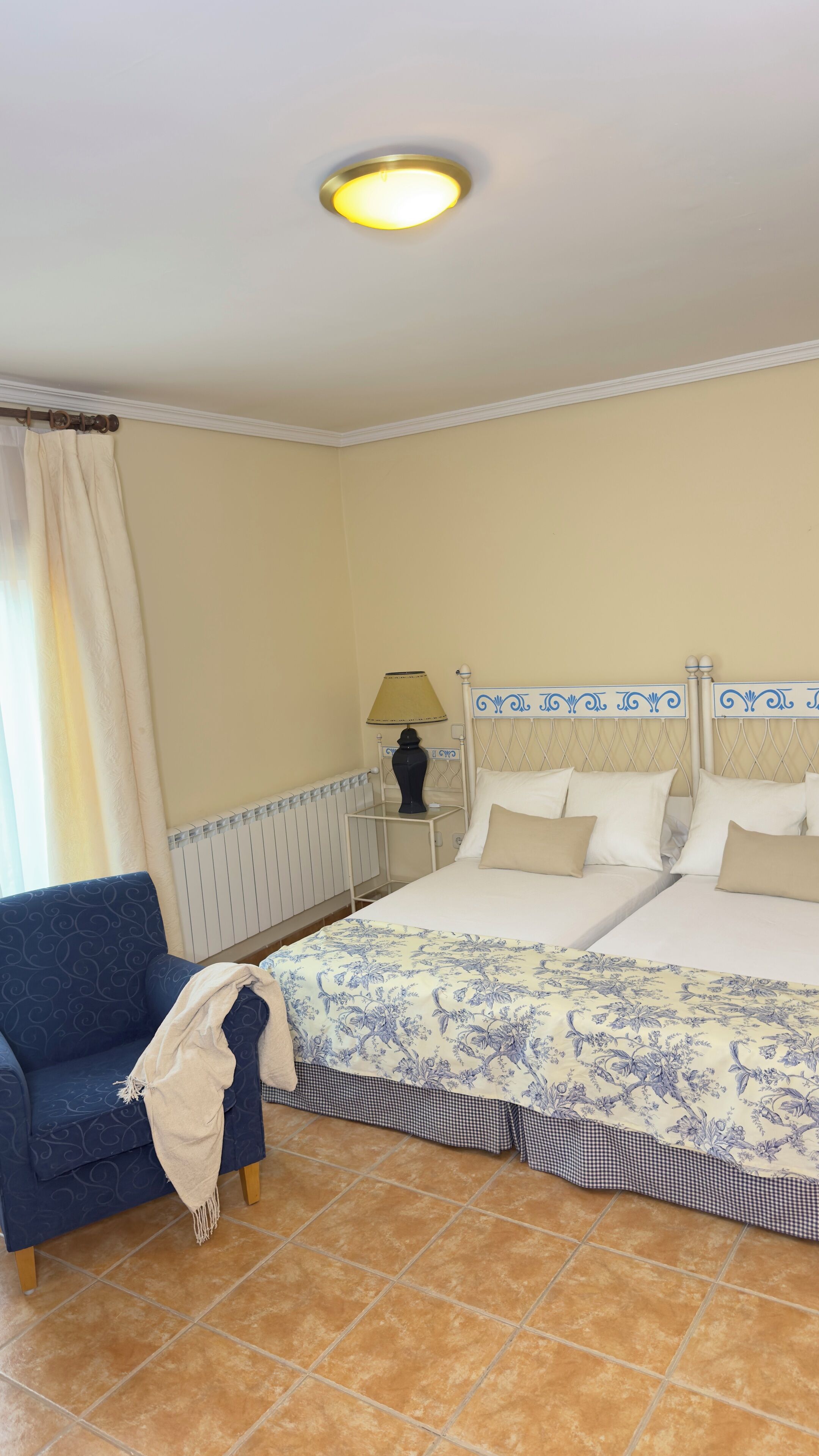 Un dormitorio con una cama doble, una mesita de noche con lámpara, un sofá azul y una ventana con cortinas.