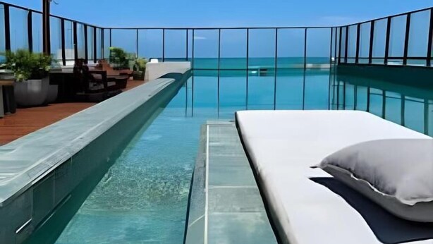 A rooftop pool with clear blue water, a lounge area with seating, and a view of the ocean. - Get one (Joao Pessoa)