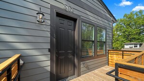 A house with a dark gray exterior, a black front door, and a wooden deck with a railing. - Stylish new build 2BR/2BA getaway w/ gated parking (Memphis)