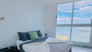 A bedroom with a bed, a nightstand, a window with a view of the sea, and a tiled floor. - The Point – Stylish 2-BR w/ Pool, Gym , Private Balcony & Free Parking (Panamá)