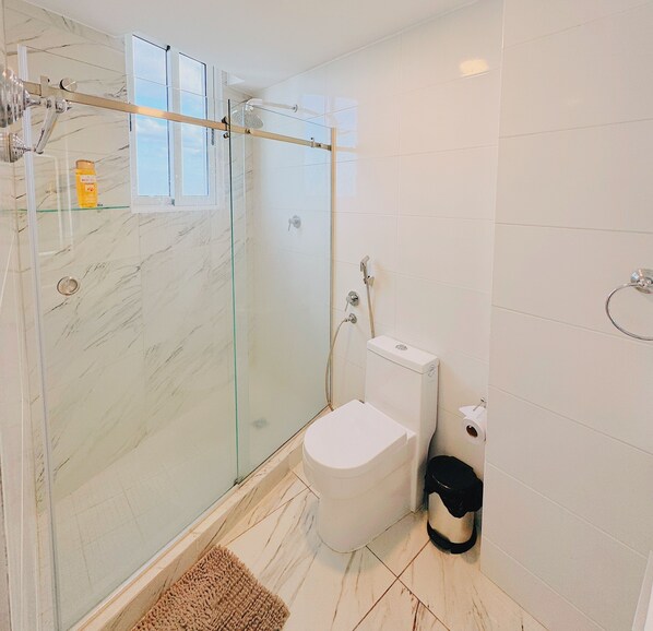 A modern bathroom with a glass-enclosed shower, a toilet, and a trash bin.