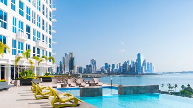 A rooftop pool with clear blue water, surrounded by lounge chairs and a city skyline in the background. - The Point – Stylish 2-BR w/ Pool, Gym , Private Balcony & Free Parking (Panamá)