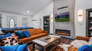 A modern living room with a pool table, leather sofa, and a fireplace. - River Front! Mini Golf! Hot Tub! Mountain views. (Sevierville)