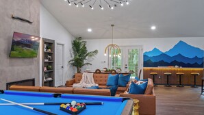 A modern living room with a pool table, a sofa, a bar area, and a mountain mural on the wall. - River Front! Mini Golf! Hot Tub! Mountain views. (Sevierville)