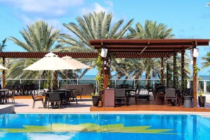 Ein Poolbereich mit einer Pergola, Sitzgelegenheiten im Freien und Palmen.