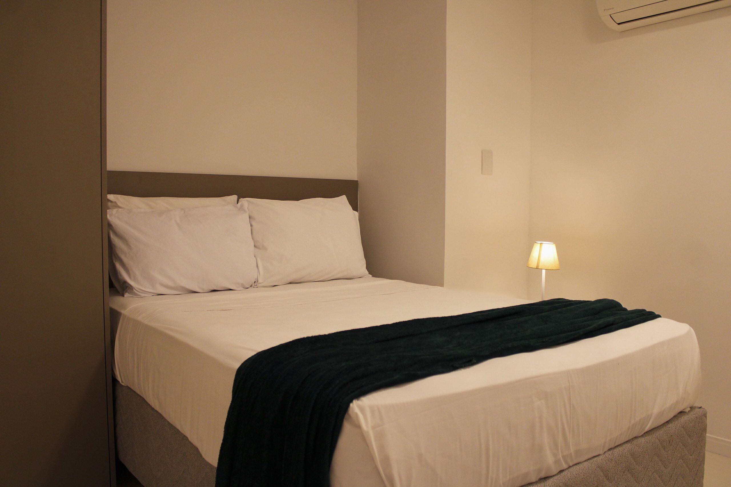 A hotel room with a bed, a nightstand, and a wall-mounted air conditioner.