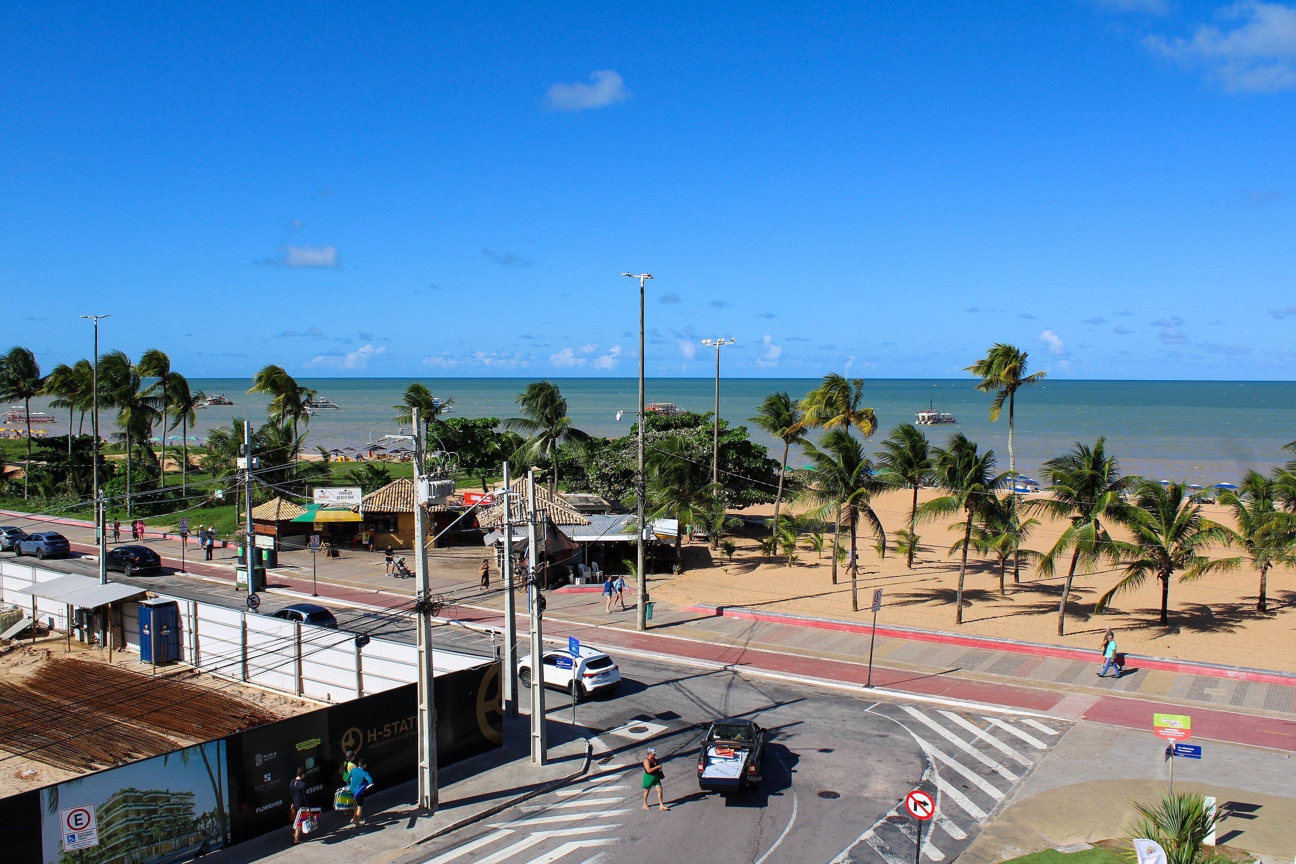 A beachside intersection with palm trees, a road, and a view of the ocean.