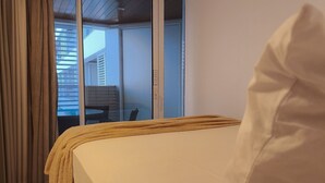 A bedroom with a bed, curtains, and a view of a balcony with a table and chairs.