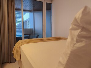 A bedroom with a bed, curtains, and a view of a balcony with a table and chairs. - Vistas Espetaculares no Solar Tambaú (Joao Pessoa)