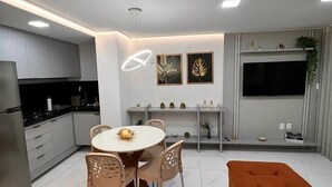 A modern kitchen with a dining area, a sofa, and a TV. - Flat Tambaú aproveite com sua família  (Joao Pessoa)