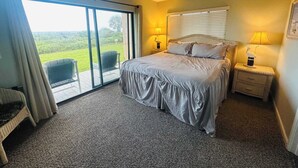 Ein Schlafzimmer mit Bett, Deckenventilator, Nachttisch mit Lampe, Sessel und Blick ins Freie.