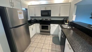 Eine kompakte Küche mit weißen Schränken, einem Edelstahlkühlschrank, einer Mikrowelle, einem Backofen und einem Spülbecken.
