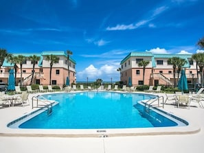 A swimming pool with lounge chairs and umbrellas, surrounded by buildings with a "NO DIVING" sign.