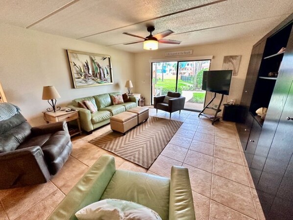 A living room with a sofa set, a coffee table, a TV, and a ceiling fan. - Oceanview 2 BR Unit 411 (St. Augustine)