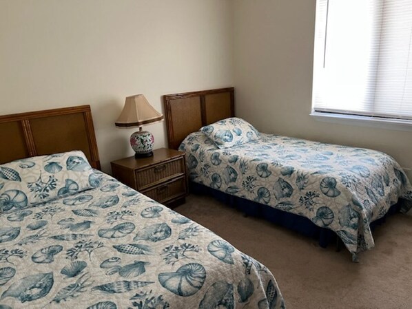 Een slaapkamer met twee bedden, een nachtkastje, een lamp en een raam met jaloezieën.