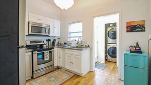 Una cocina compacta con electrodomésticos de acero inoxidable, lavadora y un refrigerador antiguo.