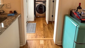 Un lavadero con dos lavadoras y secadoras apiladas, una cocina con encimeras de granito y un refrigerador verde azulado.