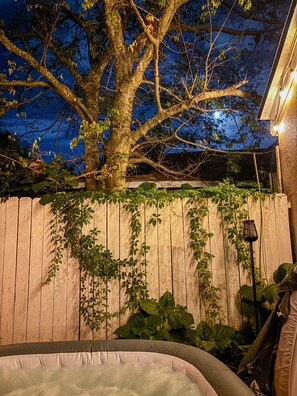 A wooden fence with climbing plants, a hot tub, and a tree with a full moon in the background.