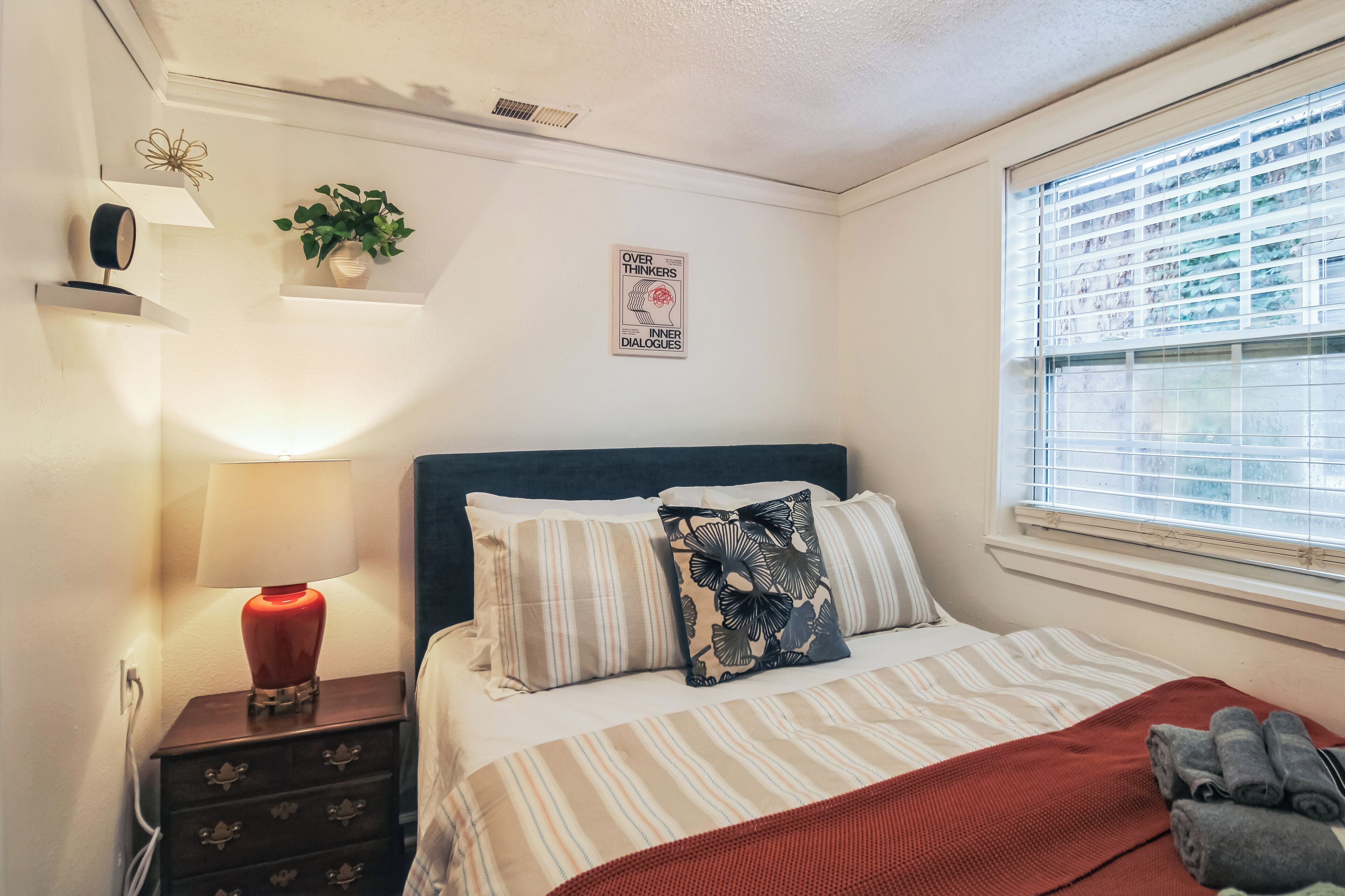 Une chambre bien rangée, avec un lit, une lampe de chevet et une fenêtre équipée de stores.