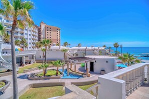 A resort with a pool, palm trees, and a view of the ocean.