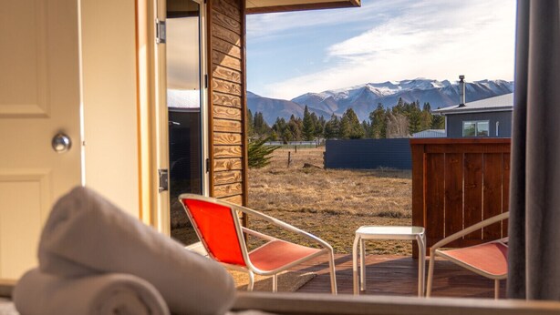 A room with a view of mountains, a wooden door, and two chairs with red cushions.