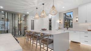 A modern kitchen with a central island, bar stools, pendant lights, and a wine rack. - The Grape Escape – Chelan Luxury Retreat w/ Spa, Hot Tub & Lake Views (Chelan)
