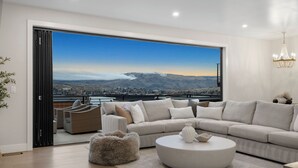 A modern living room with a large sliding glass door leading to a balcony with a city view. - The Grape Escape – Chelan Luxury Retreat w/ Spa, Hot Tub & Lake Views (Chelan)