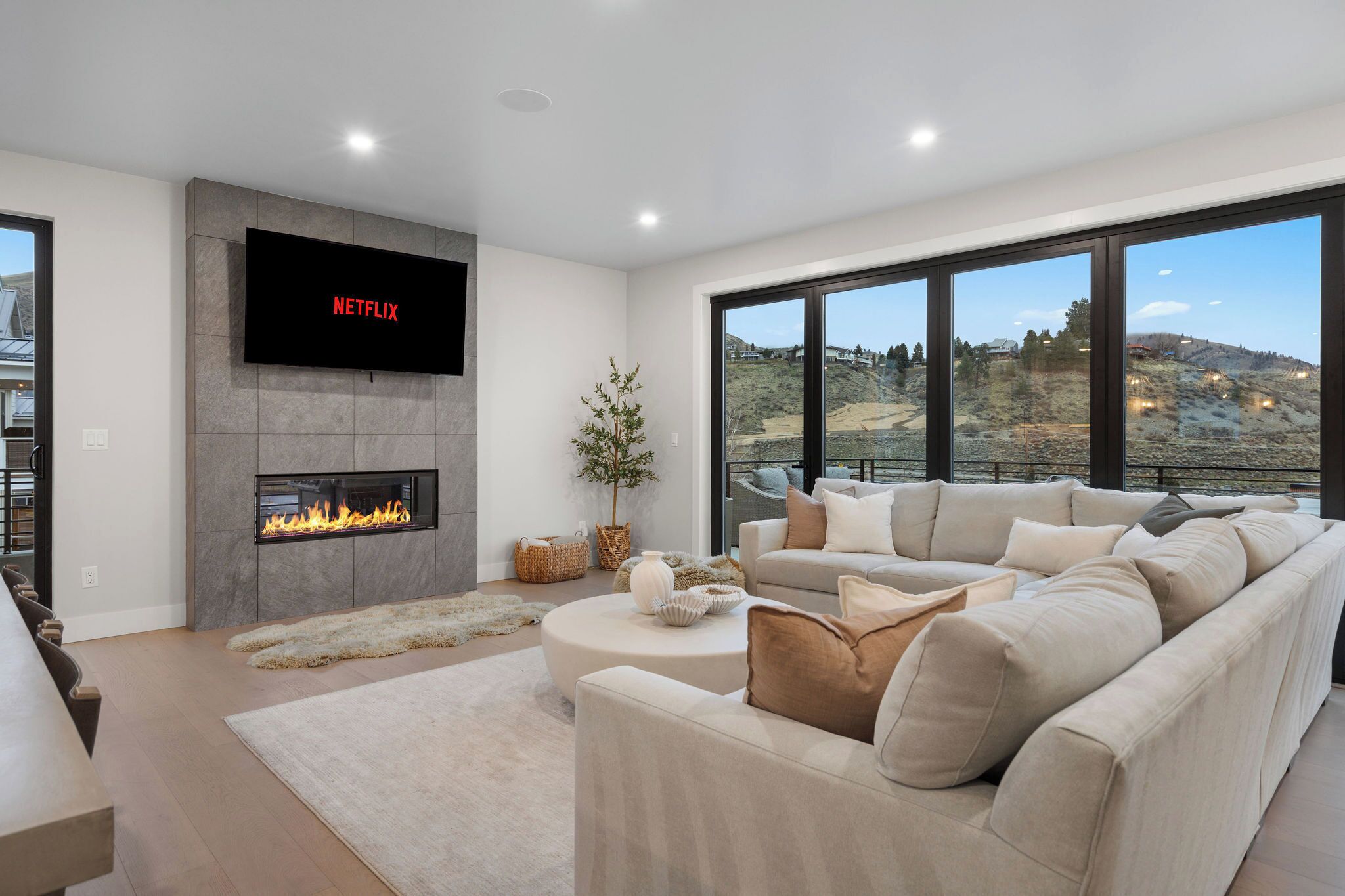 Una sala de estar moderna con chimenea, un televisor plano grande, un sofá y vistas a un paisaje montañoso a través de amplios ventanales.