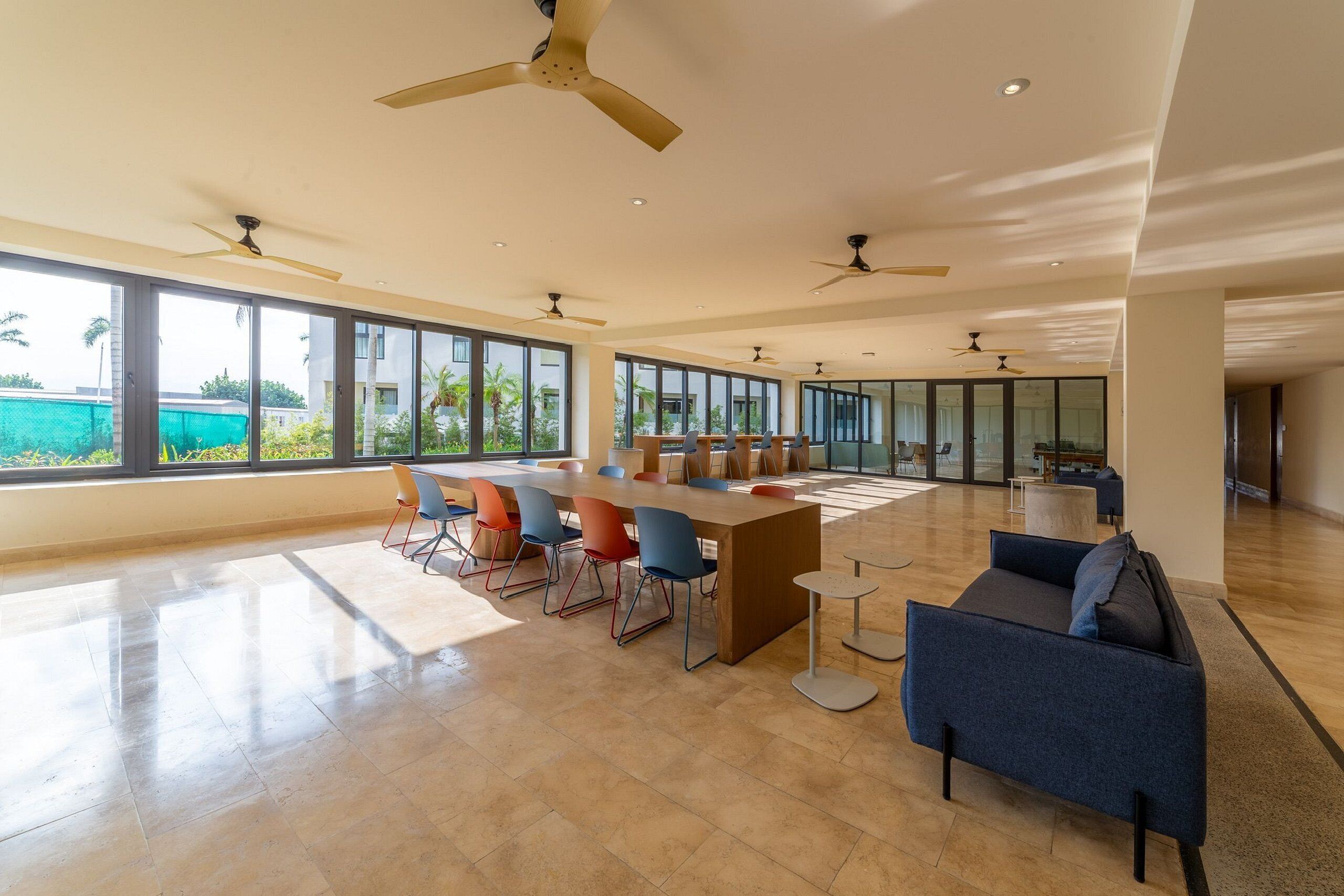 A spacious, well-lit room with a long table and chairs, large windows, and ceiling fans.