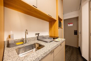 Une cuisine moderne dotée de plans de travail en granit, d’un évier en acier inoxydable et d’étagères en bois.