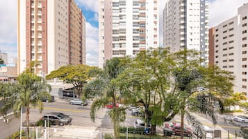 A high-rise residential building with multiple balconies, a parking area with cars, and surrounding greenery.