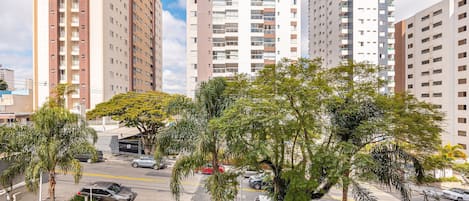 A high-rise residential building with multiple balconies, a parking area with cars, and surrounding greenery.