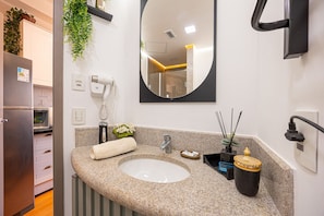A modern bathroom with a granite countertop, a sink, a mirror, a towel, a plant, and a small cabinet. - Estudios Neo Home São Caetano (Sao Caetano do Sul)