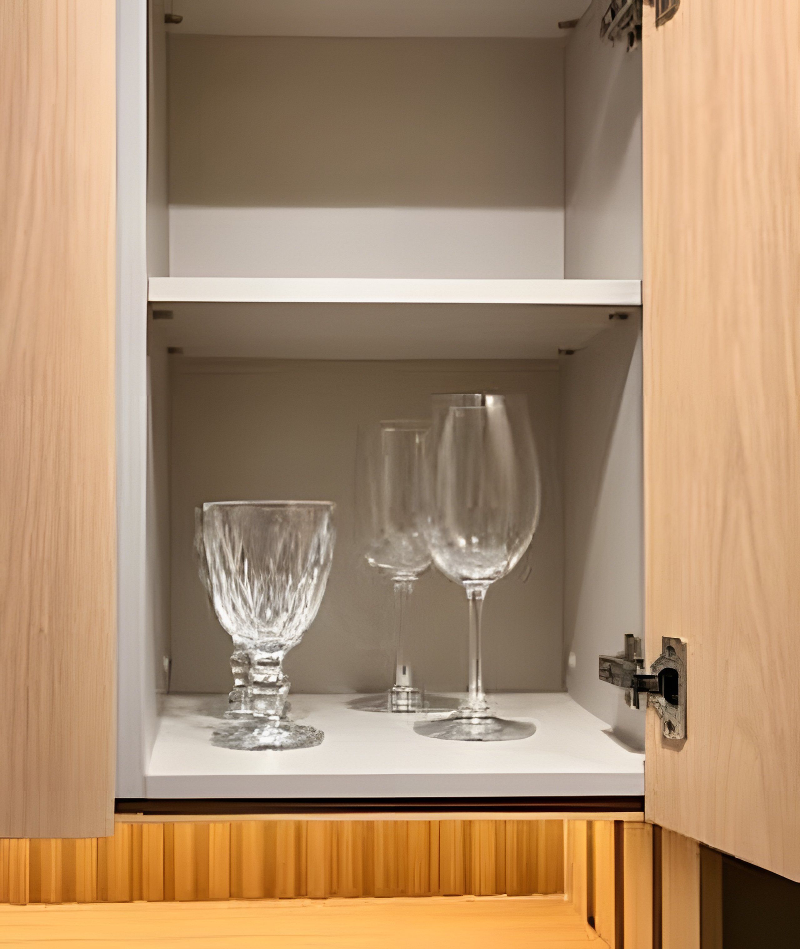 A wooden cabinet with two wine glasses and a glass bowl on a white shelf.