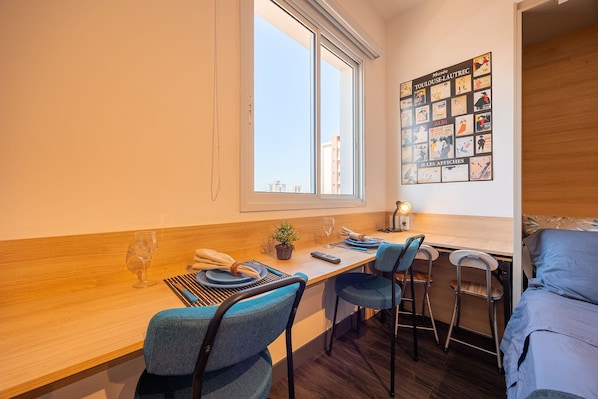 A modern room with a wooden dining table, blue chairs, a small plant, and a poster on the wall. - Estudios Neo Home São Caetano (Sao Caetano do Sul)