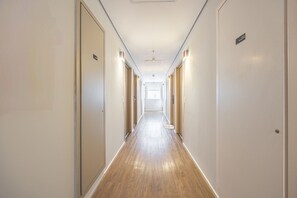 Un couloir d’hôtel avec un plancher en bois, des murs blancs et des portes de chaque côté.