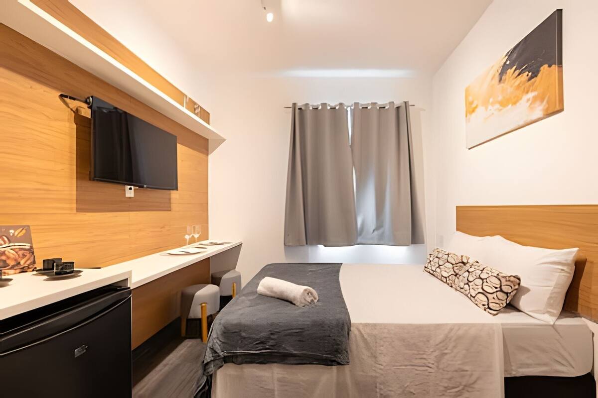 A modern hotel room with a bed, bedside table, and a flat-screen TV mounted on the wall.