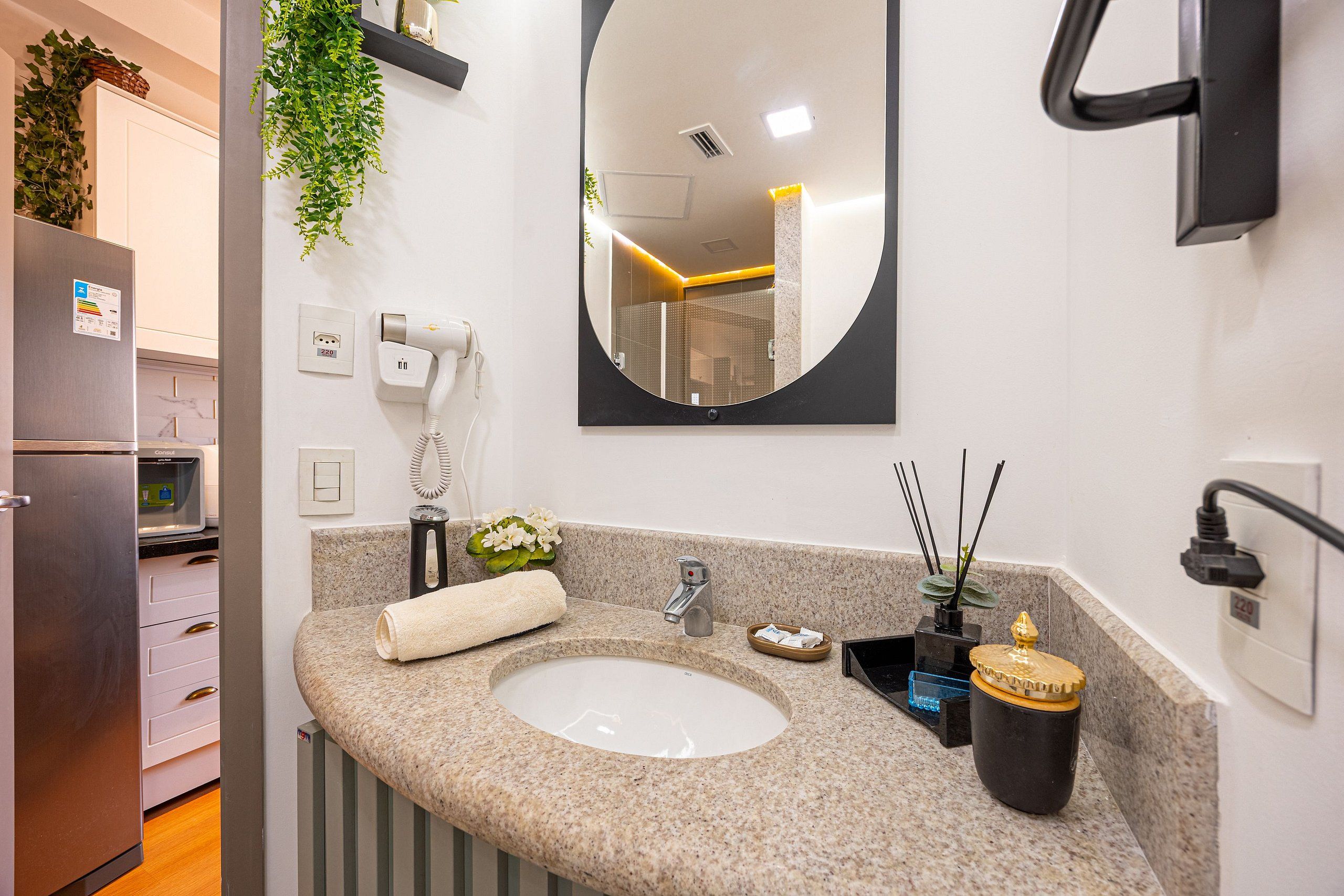 A modern bathroom with a granite countertop, a sink, a mirror, a towel, a plant, and a small cabinet.