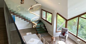 Interior moderno com escada, área de refeições e grandes janelas com vista para o verde.