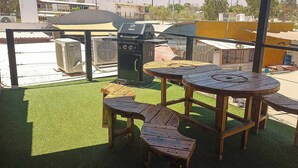 An outdoor patio with a wooden table and benches, surrounded by artificial grass. - Bottle House (San Felipe)