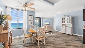 A modern living room with a dining area, a ceiling fan, a television, and a cabinet.