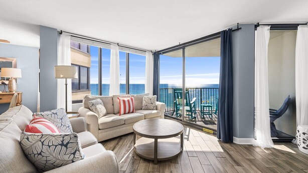 A spacious balcony with a sofa, a round coffee table, and a view of the ocean.