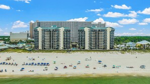 A large hotel with multiple balconies and a beach in front.